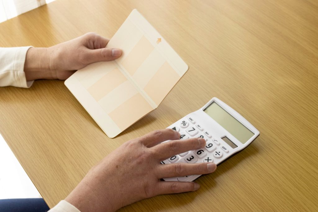 売上債権の回収予定日に入金があったかを確認するために通帳の記帳内容と電卓で照合している手元