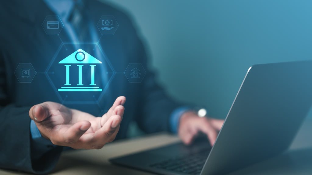 ノートPCの上の空中に浮かぶ銀行のホログラムアイコン。プロパー融資が保証協会を介さない銀行との直接取引であることを象徴するイメージ