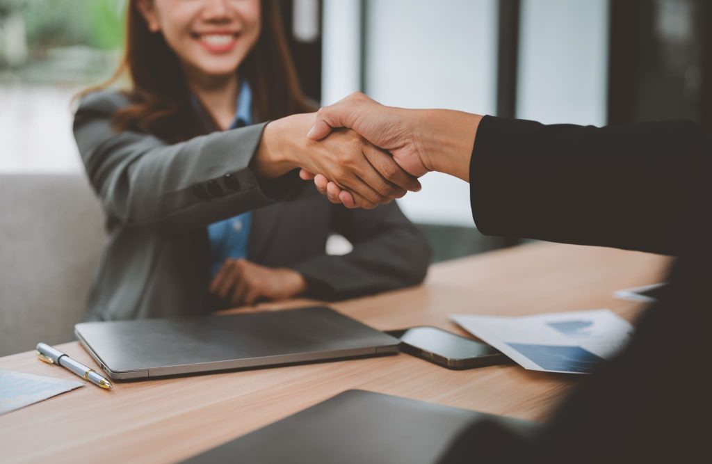 日本政策金融公庫の融資審査に通過し契約手続きを終えて担当者と笑顔で信頼の握手を交わす女性起業家