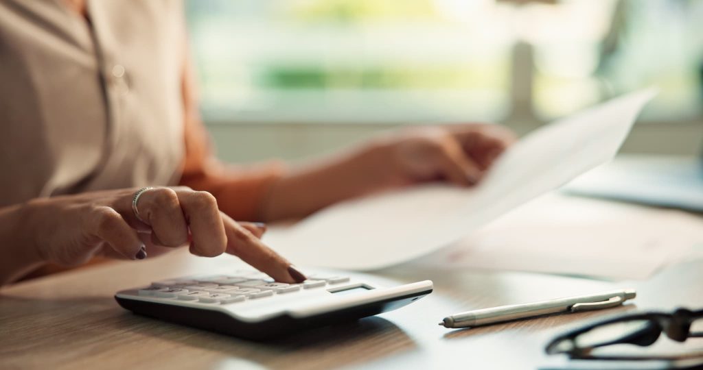 電卓をたたきながら書類を確認する女性の手元。プロパー融資の審査に必要な資金繰り表の作成や返済計画の計算を行っている経理業務