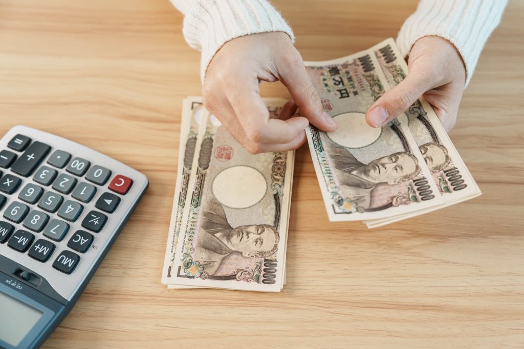 電卓の横で一万円札の束を数えている手元。助成金の受給金額を計算したり、支給によって得られる事業資金を管理している様子