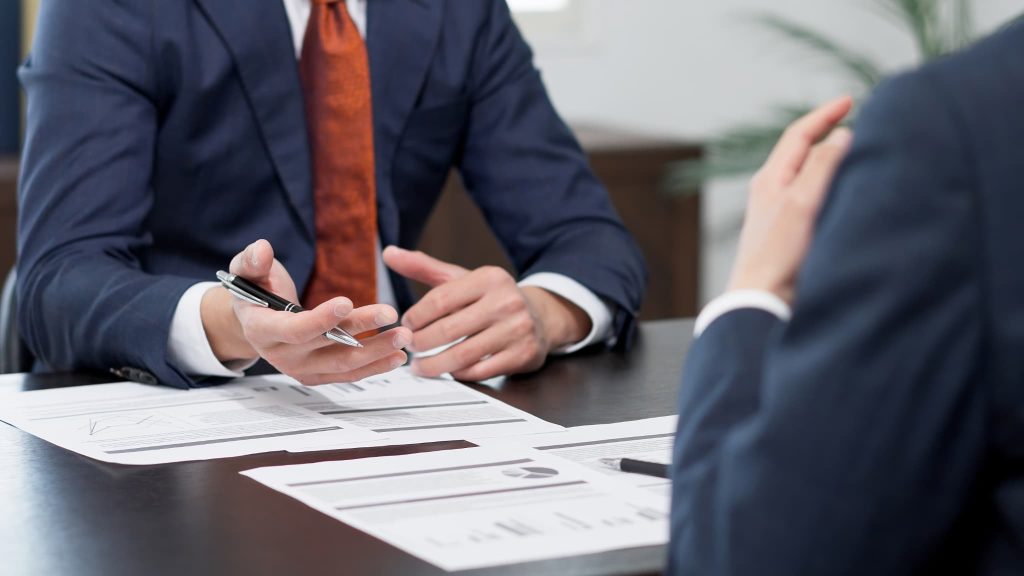 スーツを着た二人のビジネスマンが対面し、手元の資料を指し示しながら支払いサイトの条件や契約内容について商談している様子