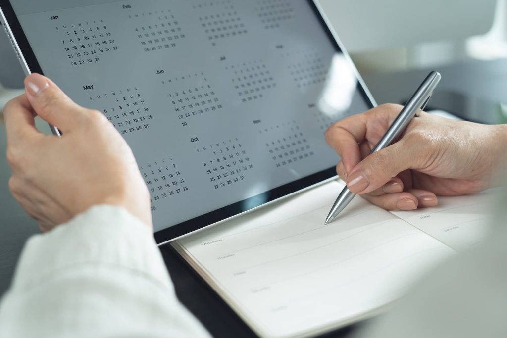タブレット端末に表示されたカレンダーにペンでスケジュールを書き込んでいる手元。ノンバンクの返済計画の管理や申し込みの日程調整を行っているビジネスシーン