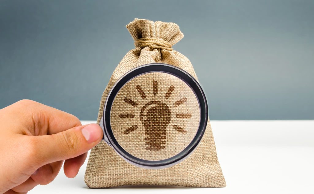 資金繰りの課題解決策として請求書カード払いサービスを見つけ出すことを表現した電球マーク入りの麻袋と虫眼鏡