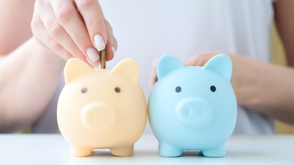 女性が2色のブタの貯金箱にコインを投入する様子。ファクタリングと手形割引の違いをイメージさせる