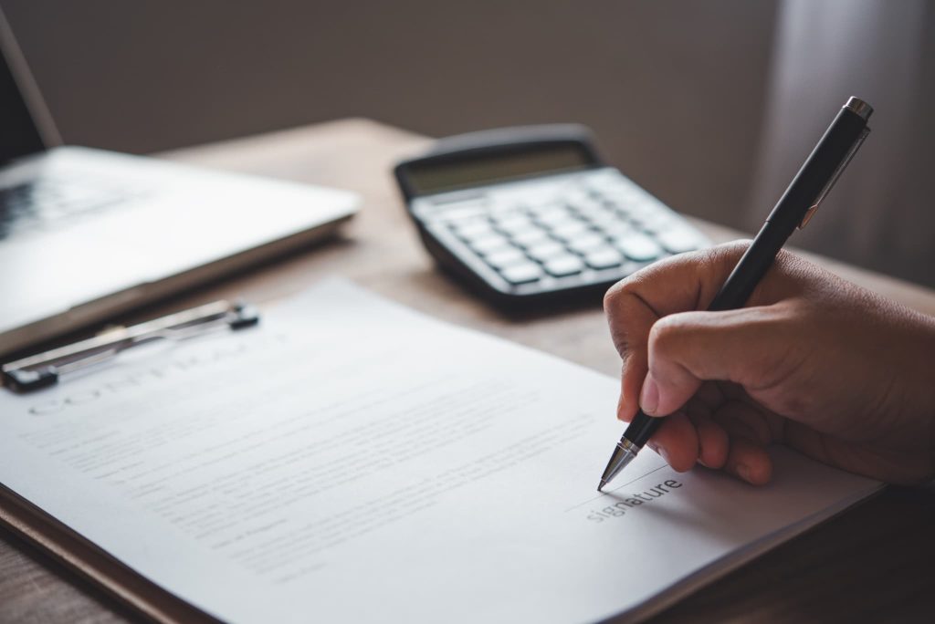 契約書の署名欄にペンでサインをしている手元のクローズアップ。審査を通過し追加融資の融資実行に向けた最終的な契約締結を行っている様子