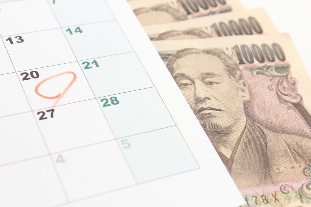 カレンダーの20日の日付にオレンジの丸印がつけられ、その横に一万円札が置かれている様子。ノンバンクからの借入や返済期日、資金繰りのスケジュール管理をイメージさせる