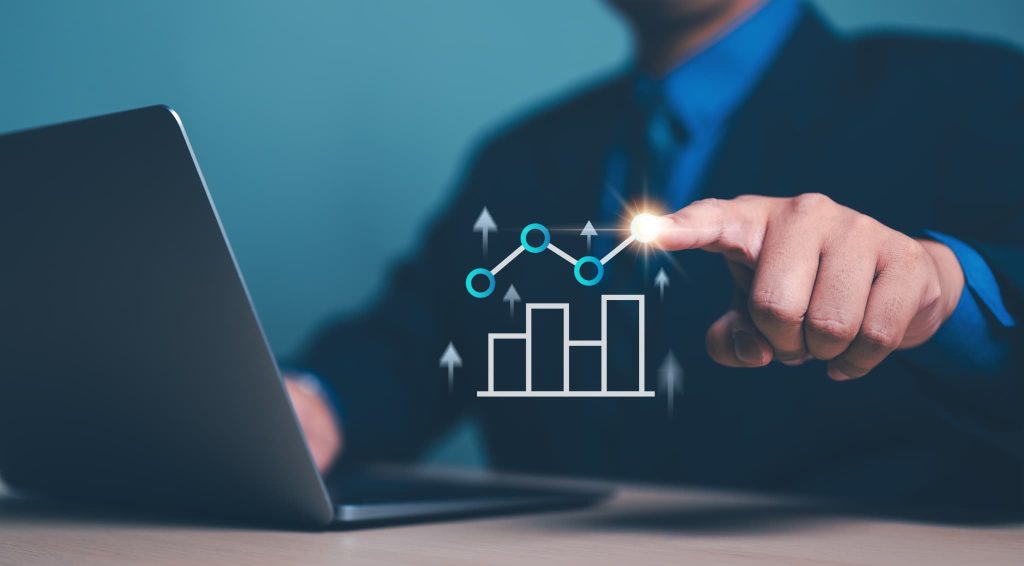 ノートパソコン上の右肩上がりのデジタルグラフを指さすビジネスマン。データに基づいた事業計画や将来の成長性を示し、スムーズに運転資金を調達するための戦略的アピール