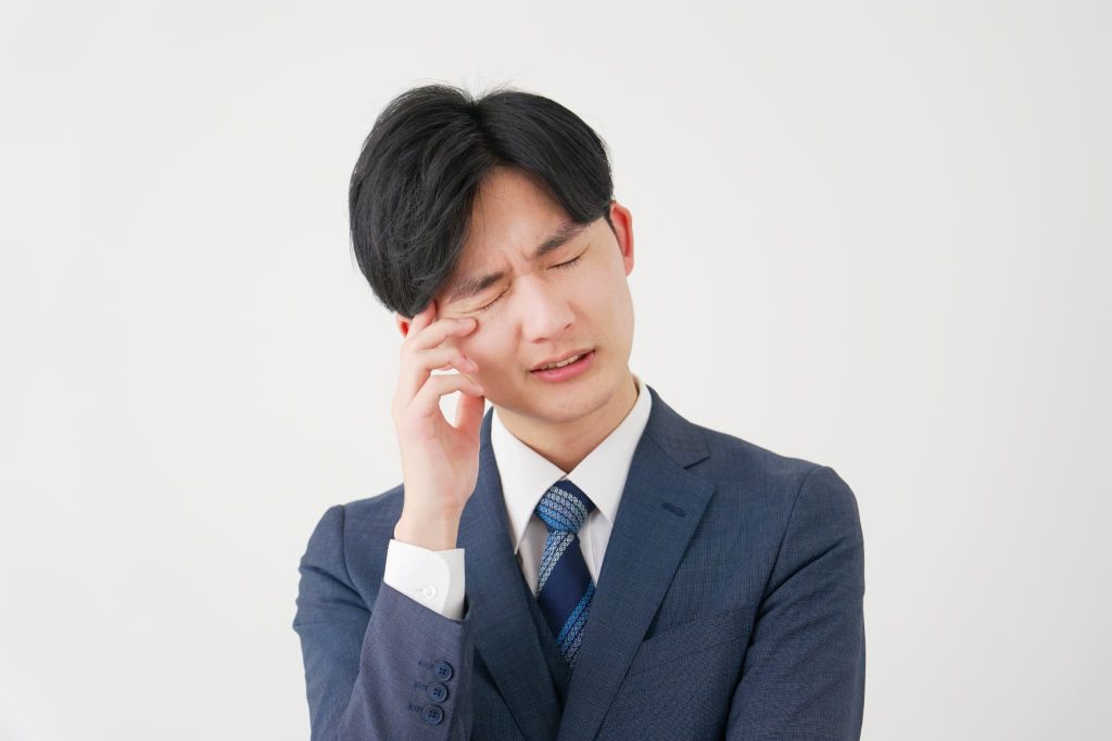 こめかみを押さえて苦渋の表情を浮かべるスーツ姿の男性。債務超過とは経営破綻の危機に瀕し、資金繰りや対応策に頭を抱えている経営者の苦悩