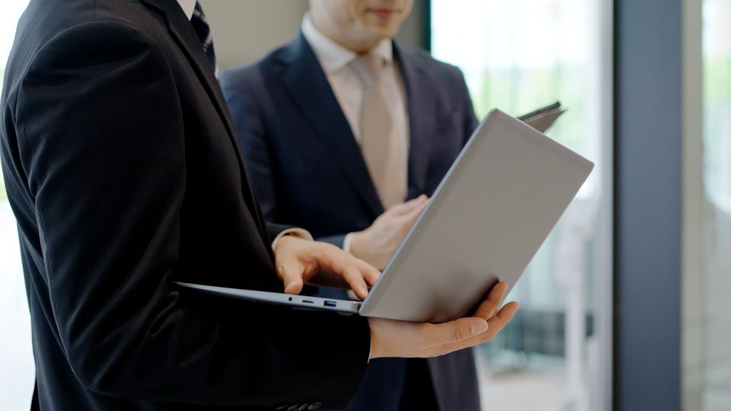 営業キャッシュフローの改善策について、ノートパソコンの画面を見せながら社内で協議するビジネスパーソン