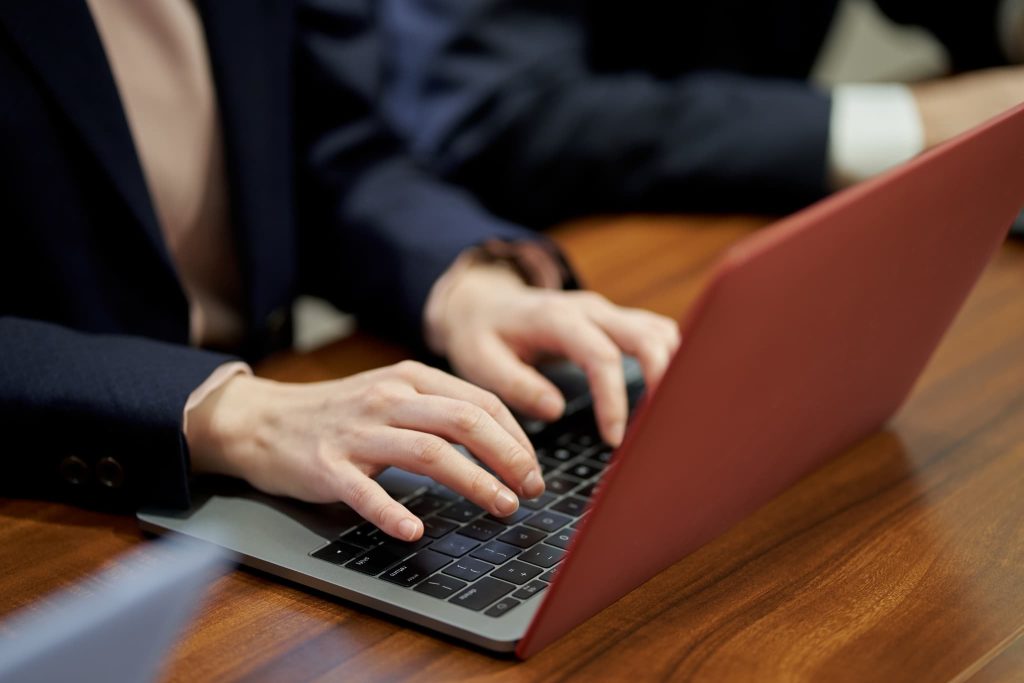 会議室で赤いノートパソコンのキーボードを打つビジネスパーソンの手元。ファクタリングの必要書類をデータ化して整理する作業風景
