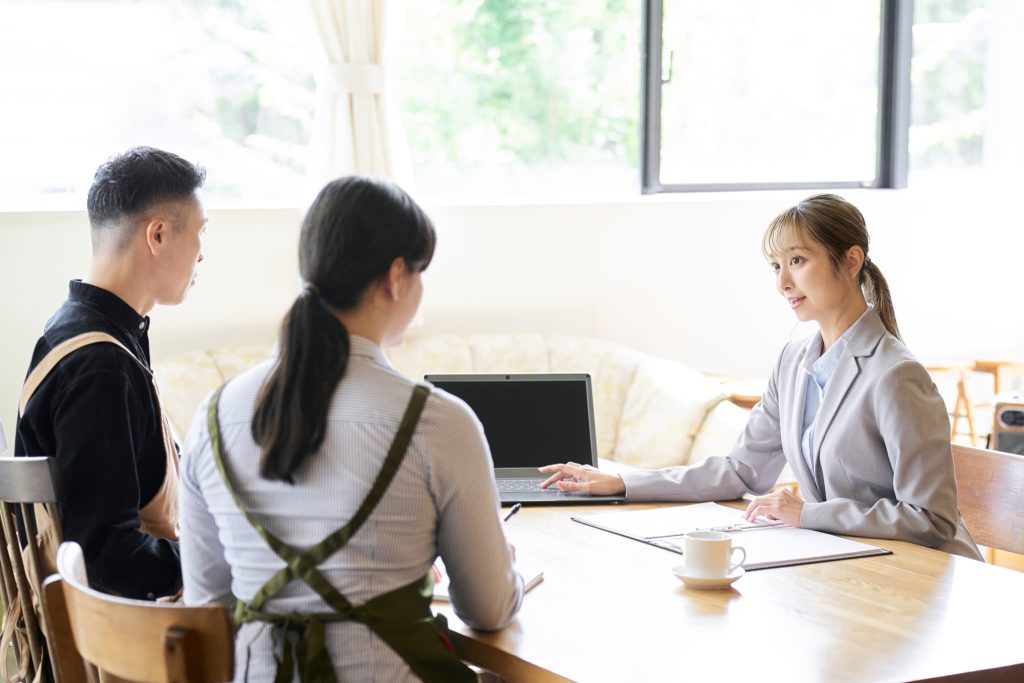 ファクタリング会社はやばい業者ではないかと懸念する飲食店の経営者たちに対面で契約内容を説明するスーツの女性