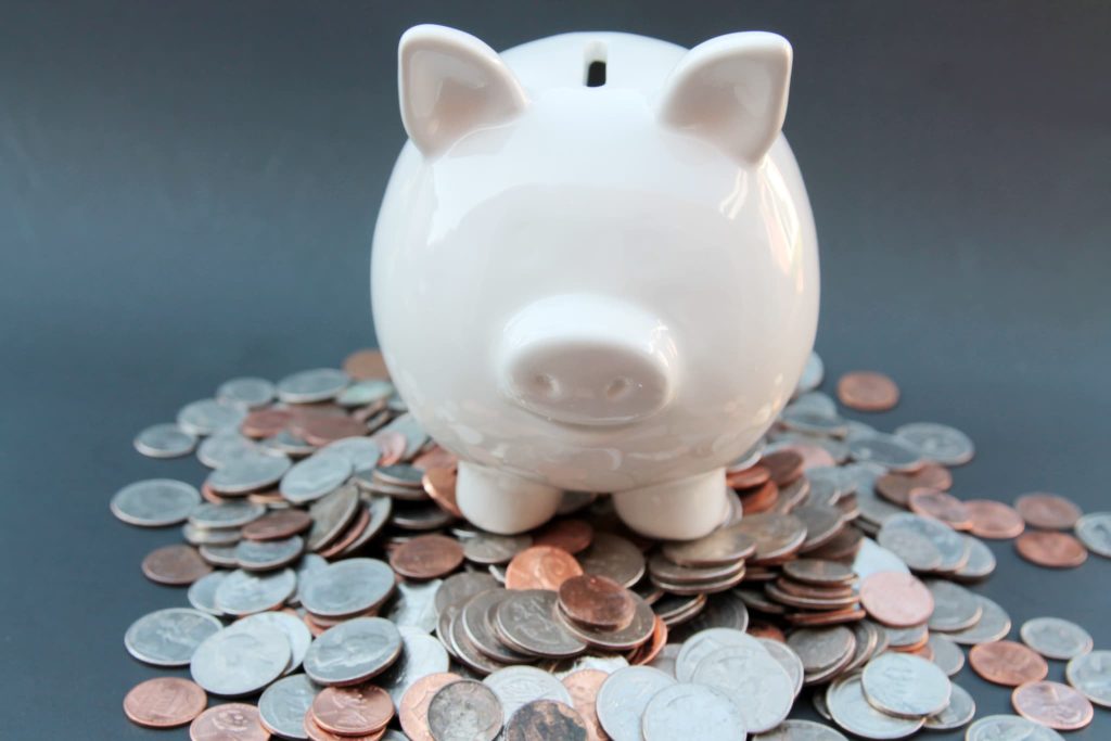 新規事業に向けた貯蓄や補助金の自己資金を表現する、大量のコインの上に置かれた白い豚の貯金箱