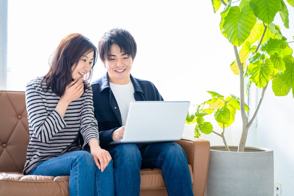 リビングで笑顔でノートパソコンを覗き込む男女。ファクタリングの必要書類を揃え終え、資金調達の目処が立ち安心している様子