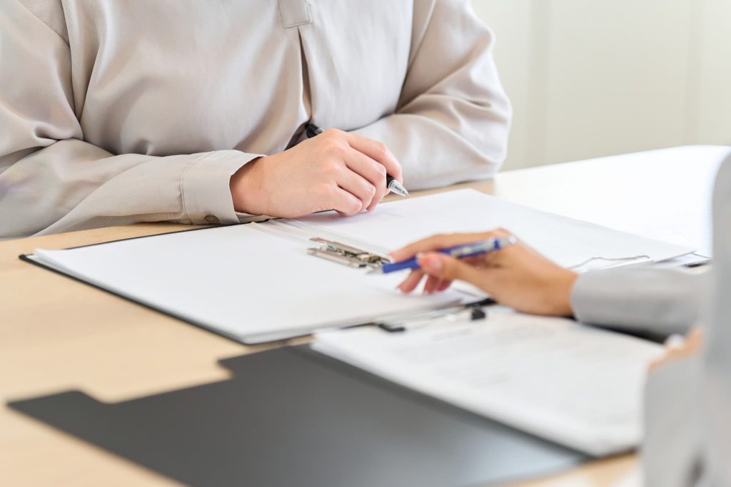 対面で書類を広げ、ペンを持って説明を聞く起業家。新創業融資制度の手続きについて金融機関の担当者や専門家からアドバイスを受けるシーン