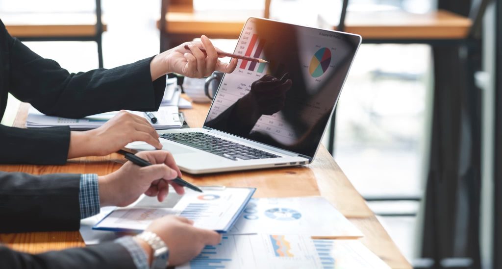 資金繰りがやばい状況を脱却するためにパソコンのグラフ画面を指差しながらファクタリングによる改善策を話し合う様子