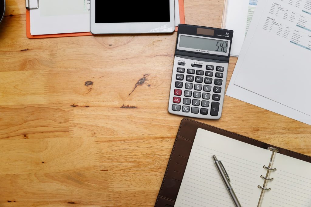 ファクタリングはやばいのか契約前にシミュレーションするために電卓や手帳などの資料が広げられた木目調のデスク