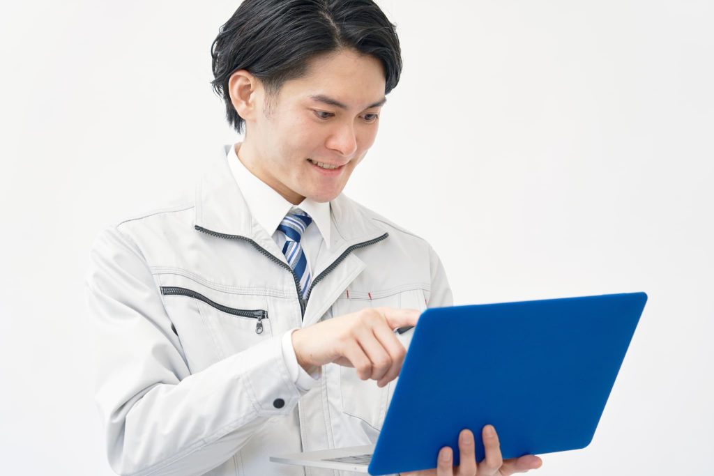 建設現場で資金繰りがやばい時期をファクタリングで乗り切り青いノートパソコンを片手に笑顔を見せる作業着の男性