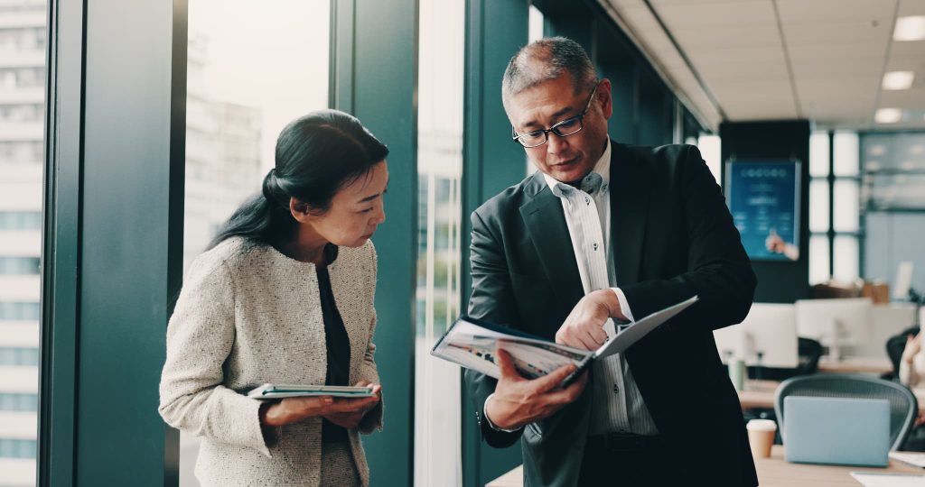 新規事業の補助金申請について、オフィスで資料を広げながら打ち合わせを行う男女のビジネスパートナー