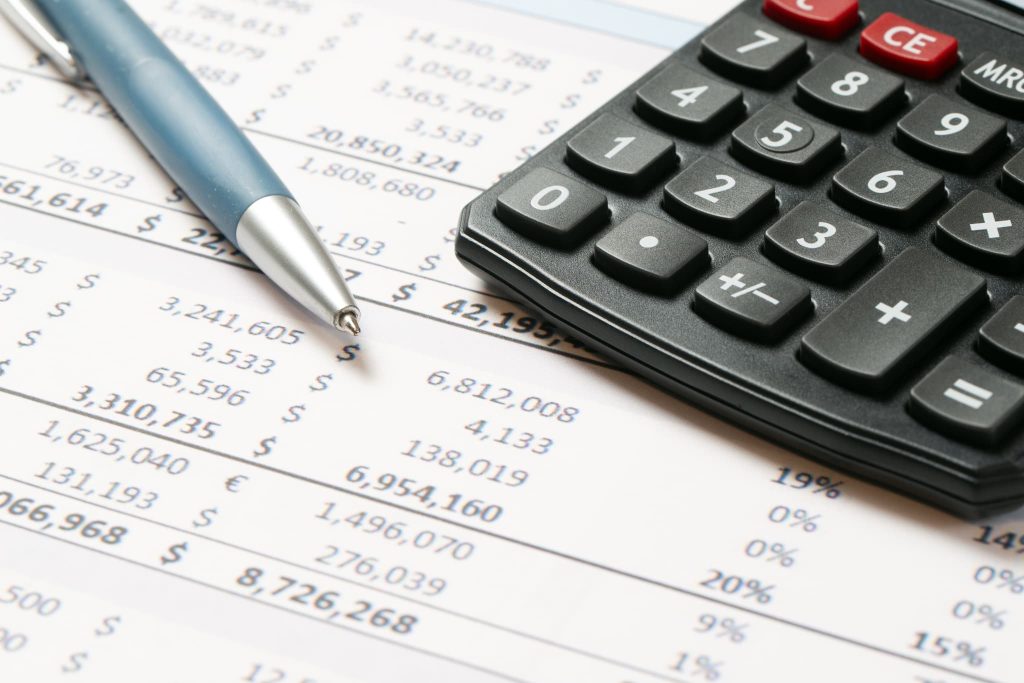 計算機とボールペンが置かれた詳細な数値の並ぶ財務書類。キャッシュフロー改善のために資金繰り表を作成し収支を細かく分析するイメージ