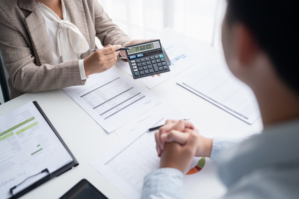 電卓に表示された1,716,830という数字を指し示す女性。開業資金の具体的な見積もり額を提示し、予算内に収まるか打ち合わせをするシーン