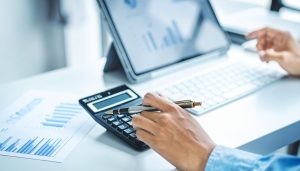 資金繰り表を作成するために電卓やタブレット、グラフ資料を用いて現金の出入りを把握し、将来の資金ショートや黒字倒産を未然に防ぐための経営判断を行う様子