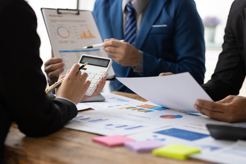 会議室で電卓と資料を手に議論するビジネスパーソン。経費削減の具体的な項目を洗い出し、数値に基づいたコストカット案を検討している様子