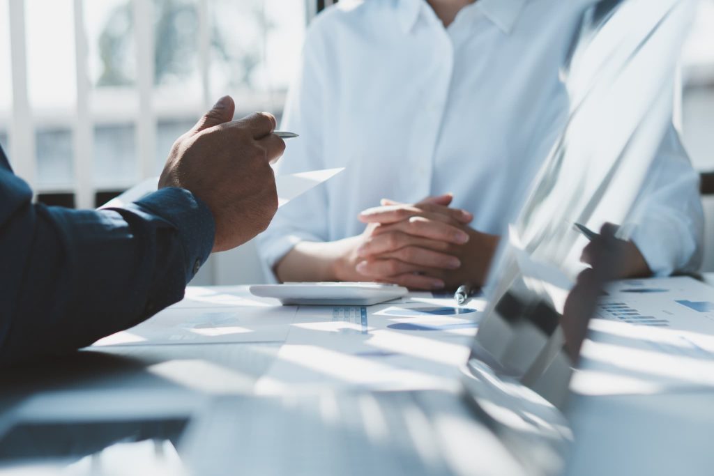 明るいオフィスで資料を広げて対面で相談する二人のビジネスパーソン。資金繰り表に基づき金融機関や専門家と資金調達の相談を行うイメージ