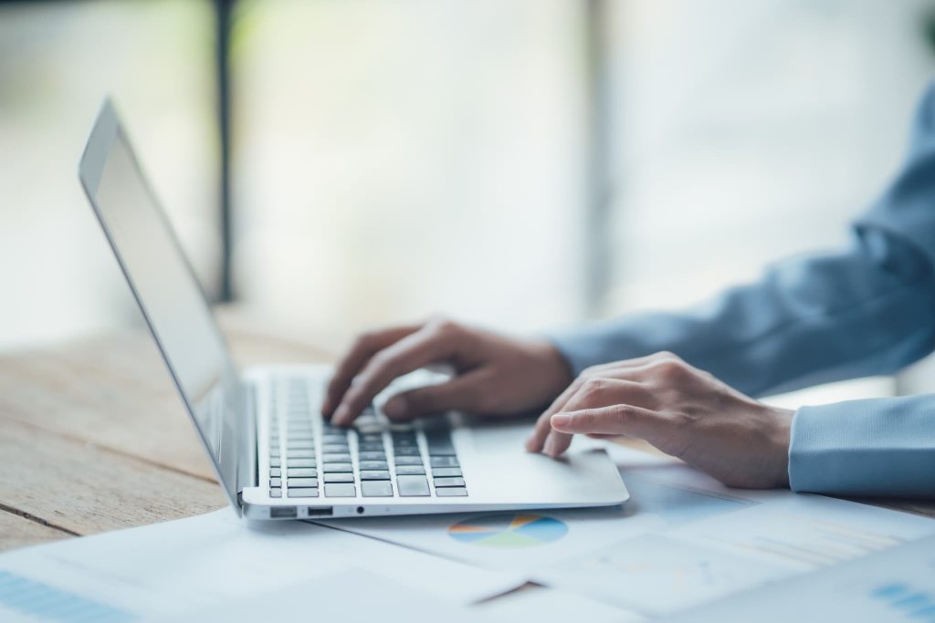 オフィスでパソコンを操作しながらグラフや資料を確認するビジネスパーソン。ファクタリングの必要書類をオンラインでアップロードする様子