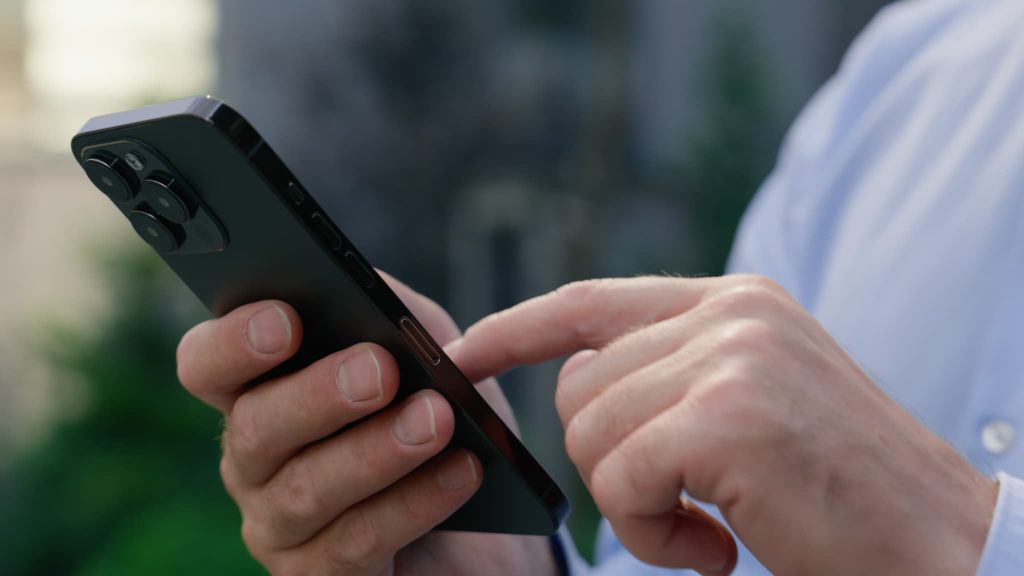 スマートフォンを操作する男性の手元のアップ。外出先でもクラウド上の資金繰り表にアクセスしリアルタイムでキャッシュバランスをチェックする様子