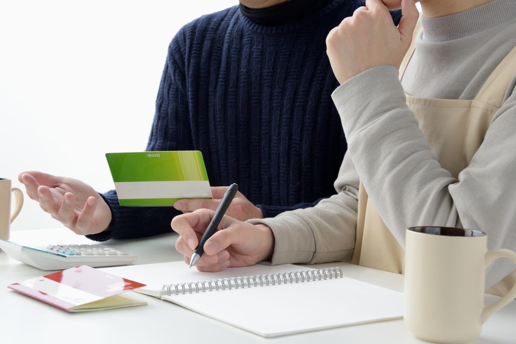 テーブルで通帳を手に持ちながらノートにペンで書き込む夫婦。新創業融資制度の申請に向けて自己資金の確認や事業計画の相談をしている様子