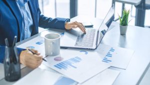 営業活動に伴う現金の収支を示す営業キャッシュフローを把握するため、パソコンやグラフ資料を用いて数値を分析し、資金繰りの改善や倒産リスク回避のための経営判断を行う様子