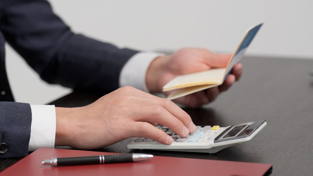 銀行融資が受けられず資金繰りがやばい中で通帳の残高を確認しながら電卓を叩いて資金調達の計算をする男性