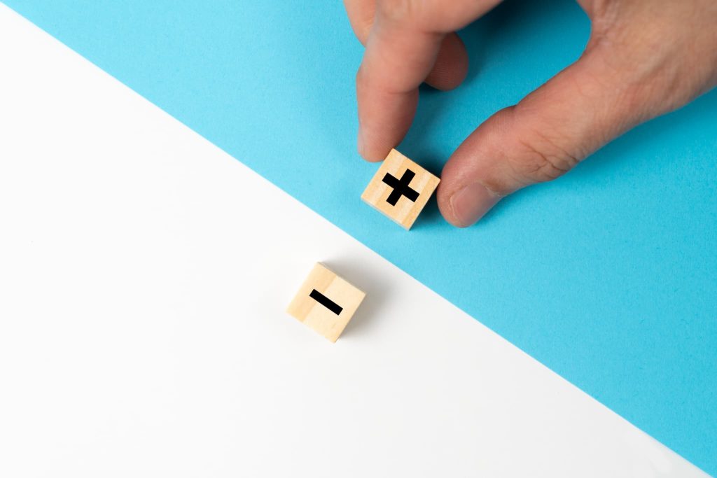 営業キャッシュフローのプラスとマイナスの増減をイメージさせる、青と白の背景に置かれたプラス・マイナス記号の木製ブロック
