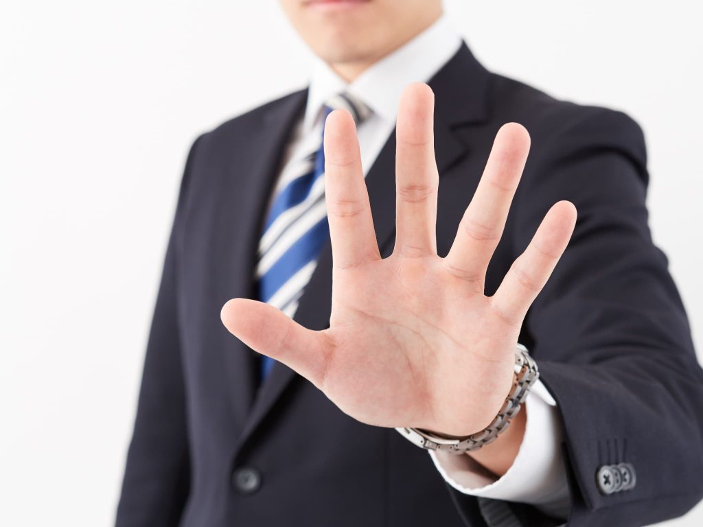 スーツ姿の男性が手のひらを前に出しストップのポーズ。無駄な支出を徹底的に排除し、経費削減を強力に推進する決意の表現