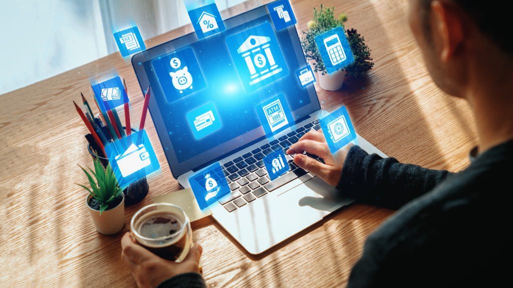 ノートパソコンの画面上に銀行や電卓などの金融アイコンが並び、資金繰りが苦しい時にオンラインで資金調達や管理を検討する男性