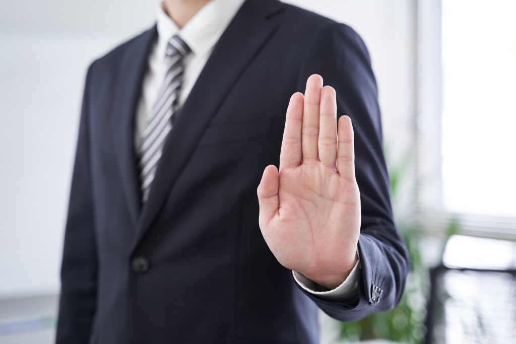 手のひらを前に出し、拒絶のポーズをとるスーツ姿の男性。ローン審査なしを謳う違法な闇金業者や悪質な勧誘を断る重要性を描写