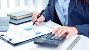 ビジネスローンのメリットである銀行融資より早い資金調達の実現に向け、電卓やグラフ資料を使って金利や調達可能額のデメリットを比較検討し、状況に応じた最適な手段を選択しようとする様子