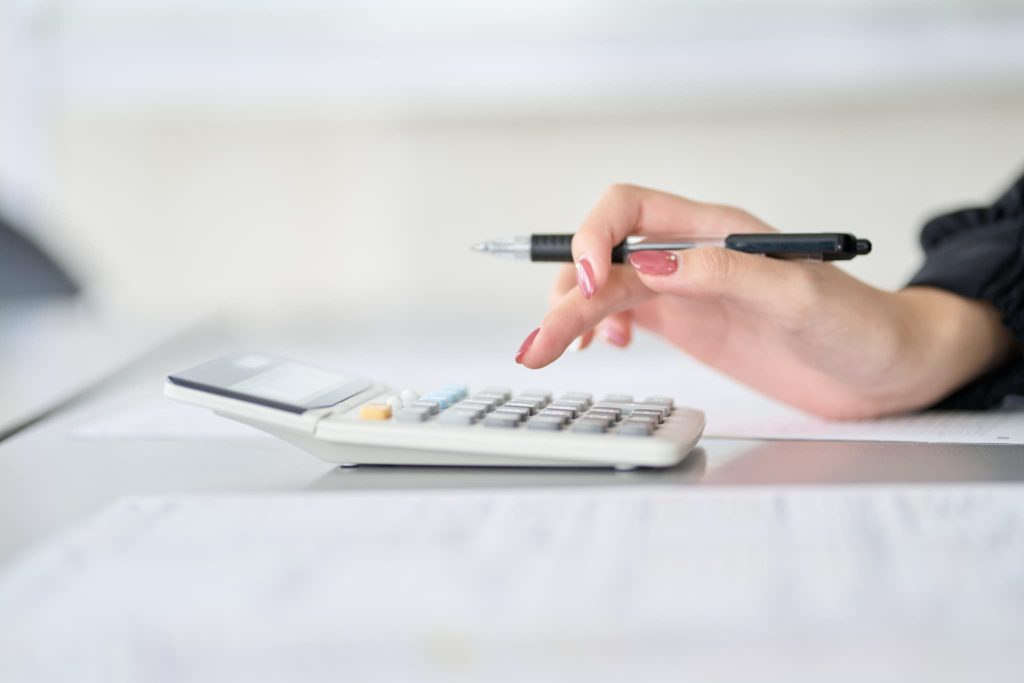 ペンを手に持ちながら電卓を操作する女性の手元。ビジネスローンの借入利息や月々の返済額をシミュレーションしている具体的なシーン