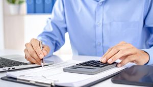 会社の収入と支出を把握・管理する資金繰りについて、電卓やパソコンを用いて収支の過不足を調整し、黒字倒産や資金不足を防ぐための具体的な改善策を検討する様子