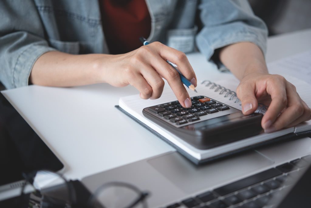 デニムシャツを着た人物が電卓とノートを使って計算に集中する手元。ビジネスローンの返済シミュレーションや資金計画の立案シーン