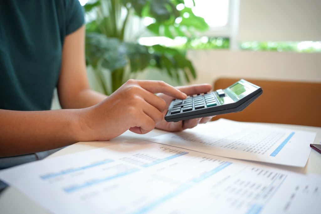 電卓を叩きながら請求書や見積書を精査する個人事業主。ファクタリングを利用して早期に回収すべき売掛金の金額を計算している様子