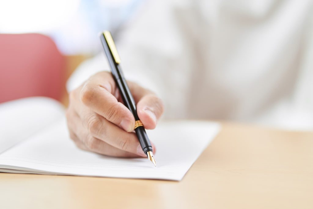 万年筆で書類に記入する手元のクローズアップ。個人事業主がファクタリング契約の申込書や契約書に署名・捺印を行うシーン