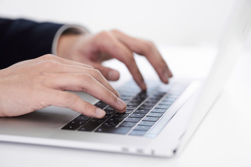 ノートパソコンのキーボードをタイピングするビジネスマンの手元。個人事業主がファクタリング会社の公式サイトからスピード審査を申し込むイメージ