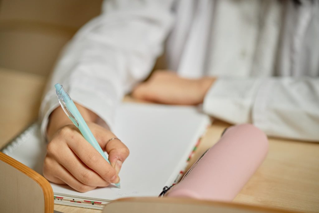 デスクでノートにペンを走らせる女性。個人事業主がファクタリングの利用計画を立てたり、資金繰りのメモを取ったりするイメージ