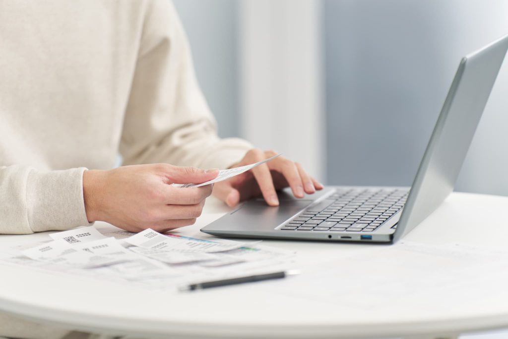 ノートパソコンを操作しながら手元の領収書や書類を確認する個人事業主。ファクタリングのオンライン申請や必要書類の準備を進める様子