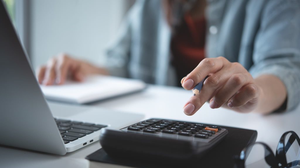 ノートパソコンを使いながら電卓で素早く計算を行う手元のクローズアップ。資金繰りとは日々の細かなキャッシュフローの把握から始まることを描写