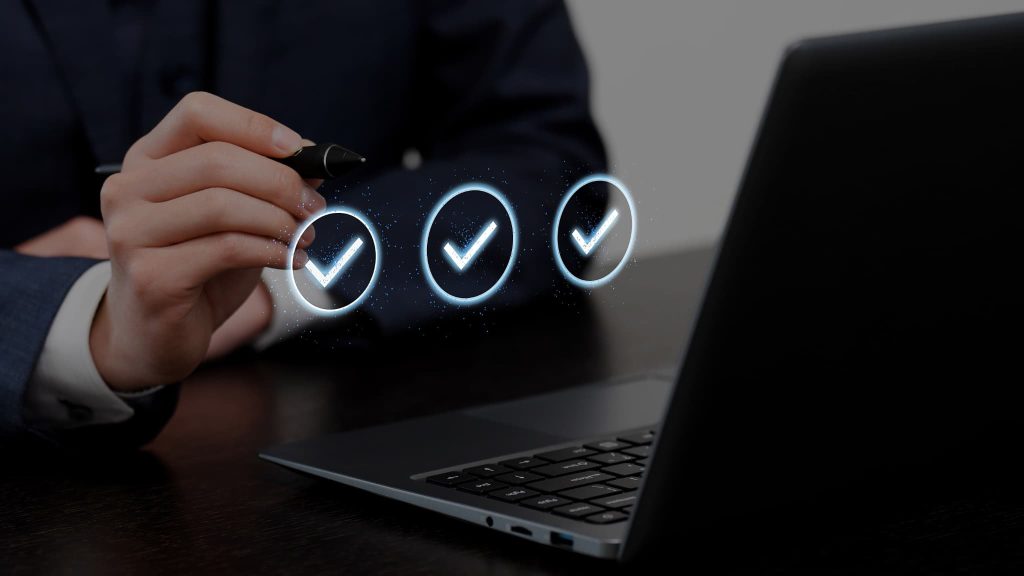ノートパソコンの前でチェックマークのホログラムを指し示す手元。少額ファクタリングの審査通過や優良業者の選定基準をチェックする様子