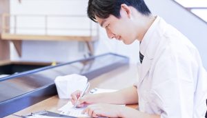 事業拡大や代金回収までの期間に欠かせない運転資金の融資を受けるため、政府系金融機関や銀行への相談に向けて説得力のある事業計画書を店舗のカウンターで真剣に作成する様子