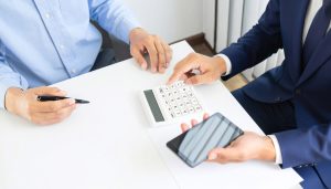 銀行融資よりも融資スピードが早い法人向けビジネスローンのメリットを活かし、急な資金需要に備えて電卓やスマホで借入条件をシミュレーションしながら資金調達の相談を行う様子